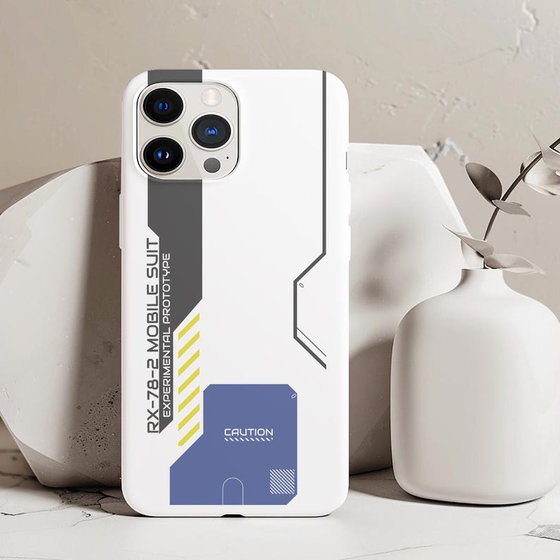 May include: White phone case with a black and gray design. The case has a graphic of a robot with the text "RX-78-2 MOBILE SUIT EXPERIMENTAL PROTOTYPE" and "CAUTION".