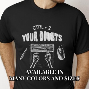 May include: Black t-shirt with white text that reads "CTRL + Z YOUR DOUBTS". The shirt also features a keyboard, mouse, and two hands typing. The text "AVAILABLE IN MANY COLORS AND SIZES" is at the bottom of the shirt.