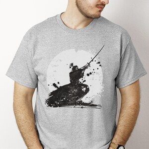 K&ouml;nnte beinhalten: Hellgraues T-Shirt mit einer Schwarz-Wei&szlig;-Tuscheillustration eines Samurai-Kriegers in Aktion. Das Design umfasst einen wei&szlig;en kreisf&ouml;rmigen Hintergrund und schwarze Farbspritzer, die einen dynamischen und k&uuml;nstlerischen Look erzeugen.