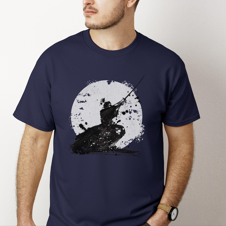 K&ouml;nnte beinhalten: Marineblaues T-Shirt mit einer Schwarz-Wei&szlig;-Illustration eines Samurai in Aktion. Das Design zeigt einen Samurai vor einem gro&szlig;en wei&szlig;en Kreis mit schwarzen Spritzereffekten, was einen dramatischen Effekt erzeugt.