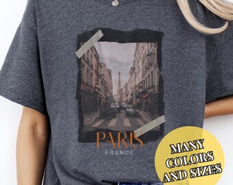 May include: A dark gray t-shirt with a graphic print of a street scene in Paris, France. The graphic includes the Eiffel Tower and the text "Paris, France".