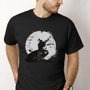 K&ouml;nnte beinhalten: Schwarzes T-Shirt mit einer schwarz-wei&szlig;en Grafik eines Samurai-Kriegers vor einem wei&szlig;en Kreis, der an einen Mond erinnert. Der Samurai ist mit einem Schwert dargestellt. Das Design ist in Schwarz und Wei&szlig; gehalten.