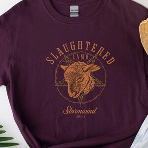 May include: Dark purple t-shirt with a graphic of a lamb's head inside a star and circle, with the words "SLaughtered Lamb" above and "Stormwind 2004" below in a serif font. The shirt is made of heavy cotton.