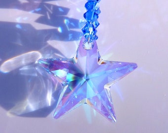 May include: A blue crystal star with iridescent facets hangs from a blue crystal prism. The star is a five-pointed star with a clear centre. The prism is made of faceted crystals and is attached to a silver chain.
