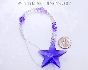 May include: A purple crystal star suncatcher with a clear crystal beaded chain. The suncatcher is hanging from a silver wire. The suncatcher is about the size of a UK ten pence coin.