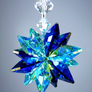 May include: A faceted, star-shaped crystal ornament in shades of blue and green, suspended by a clear beaded strand. The ornament's multiple facets reflect light, creating a sparkling effect. The text "&copy; LILLI HEART DESIGNS 2013" is visible at the top.