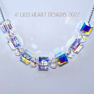Könnte beinhalten: Eine silberne Kettenkette mit regenbogenfarbenen Kristallperlen. Die Perlen sind quadratisch und rechteckig geformt. Die Kette liegt auf einem weißen Hintergrund. © Lilli Heart Designs 2022