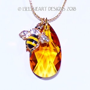 May include: A gold chain necklace with a teardrop-shaped amber crystal pendant and a small bee charm with black and yellow stripes and clear rhinestones.