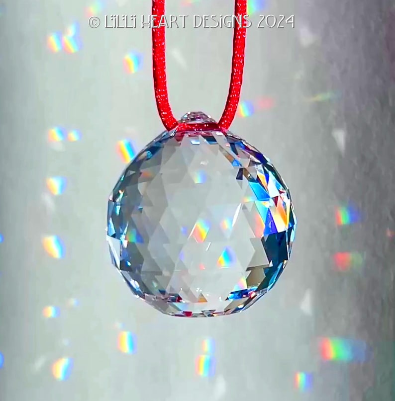 May include: A clear crystal ball hanging from a red cord. The ball is faceted and casts rainbows on the background.