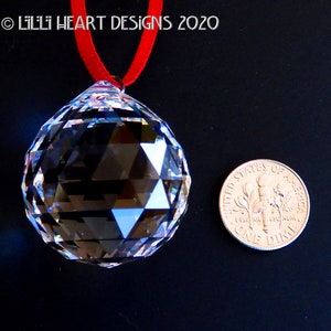 May include: A clear crystal ball with a faceted design, hanging from a red ribbon. The ball is about the size of a US dime.