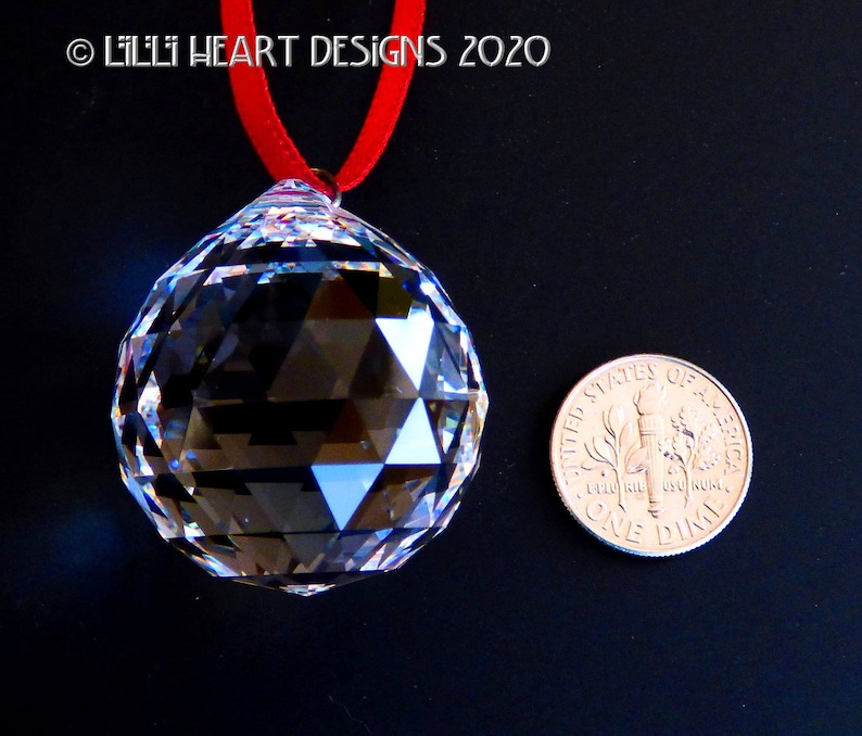 May include: A clear crystal ball with a faceted design, hanging from a red ribbon. The ball is about the size of a US dime.