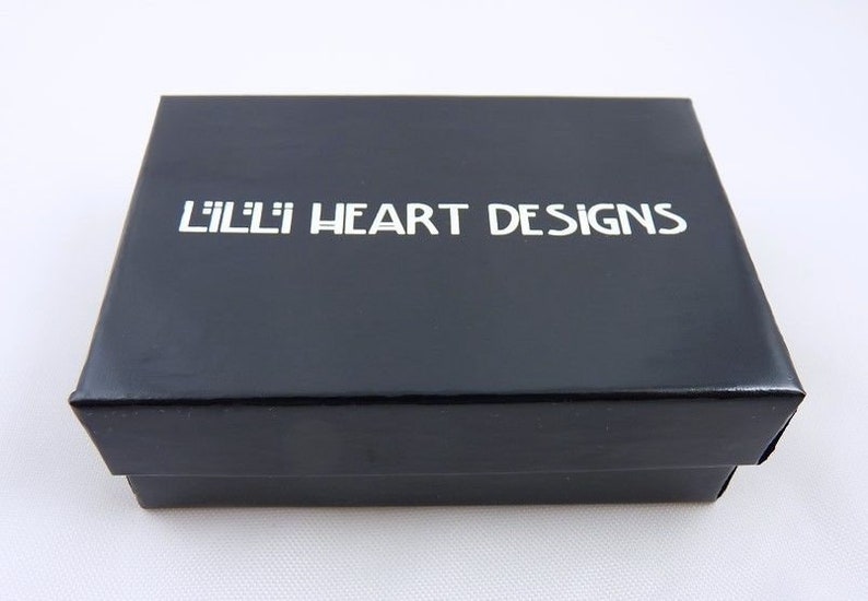Puede incluir: Una caja negra con el texto "Lilli Heart Designs" impreso en blanco.