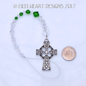 May include: A silver Celtic cross charm with a clear crystal in the center, hanging from a clear crystal beaded chain with green crystal accents.  The charm is about the size of a US dime.