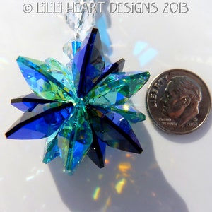 May include: A faceted crystal starburst ornament in shades of blue and green, with a silver dime for size comparison. The ornament is suspended from a clear beaded strand. The image is well-lit, showcasing the crystal's reflective qualities.