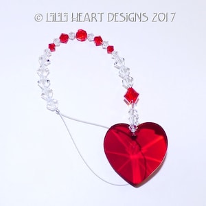 May include: A red crystal heart hanging from a crystal and red bead chain. The chain is attached to a white string. The text "Lil'Lil HEART DESIGNS 2017" is visible in the top left corner of the image.