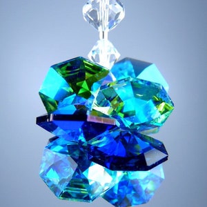 May include: A cluster of faceted crystal beads in shades of blue, green, and clear. The crystals are arranged in a layered design, reflecting light and creating a sparkling effect. The text "&copy; LILLI HEART DESIGNS 2013" is visible at the top.