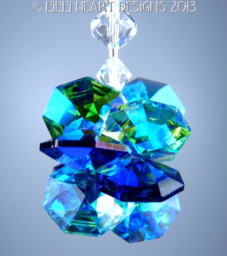 May include: A cluster of faceted crystal beads in shades of blue, green, and clear. The crystals are arranged in a layered design, reflecting light and creating a sparkling effect. The text "&copy; LILLI HEART DESIGNS 2013" is visible at the top.