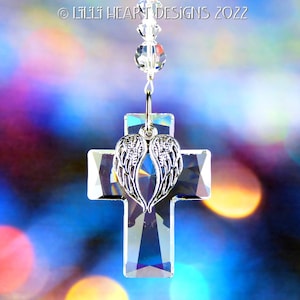 Puede incluir: Cruz de cristal con alas de ángel en un diseño de corazón que cuelga de una cadena de cuentas de cristal. La cruz es transparente y las alas son plateadas. El fondo está desenfocado y fuera de foco.