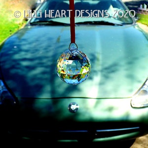 May include: A green car with a crystal ball hanging from the rearview mirror. The crystal ball is reflecting light and creating a rainbow effect.