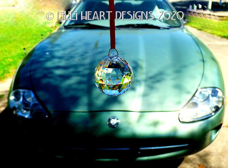 May include: A green car with a crystal ball hanging from the rearview mirror. The crystal ball is reflecting light and creating a rainbow effect.