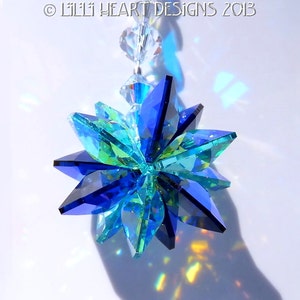 May include: A faceted crystal suncatcher with a starburst design. The suncatcher features shades of blue and green, with clear crystal beads at the top. The text "&copy; LILLI HEART DESIGNS 2013" is visible at the top.