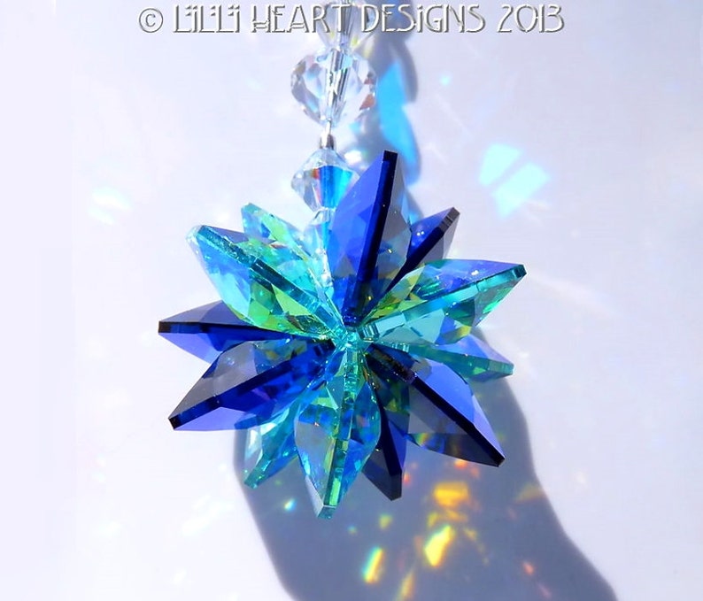 May include: A faceted crystal suncatcher with a starburst design. The suncatcher features shades of blue and green, with clear crystal beads at the top. The text "&copy; LILLI HEART DESIGNS 2013" is visible at the top.
