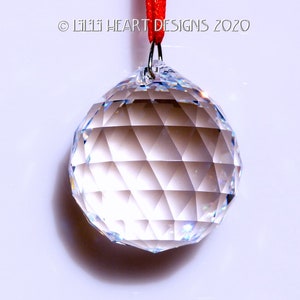 May include: A clear crystal ball with a faceted surface hangs from a red string.  The ball is approximately 2 inches in diameter.  &copy; Lilli Heart Designs 2020
