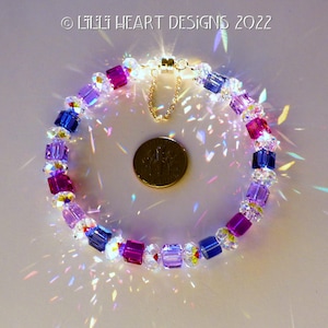 Könnte beinhalten: Ein mehrfarbiges Kristall-Armband mit einem goldenen Verschluss. Das Armband besteht aus quadratischen Kristallen in den Farben Lila, Blau und Rosa. Das Armband liegt auf einer weißen Oberfläche.