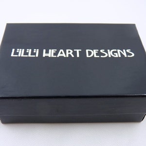 May include: A black rectangular box with the text "LILLI HEART DESIGNS" in white lettering on the lid. The box is glossy and appears to be made of cardboard or a similar material. The background is white.