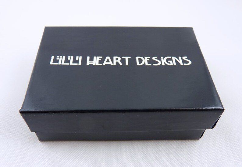 May include: A black rectangular box with the text "LILLI HEART DESIGNS" in white lettering on the lid. The box is glossy and appears to be made of cardboard or a similar material. The background is white.