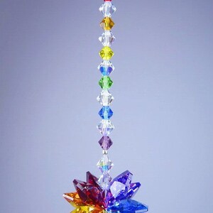 Puede incluir: Un atrapasol de cristal arco&iacute;ris con una cadena de cristal colgando de la parte superior. El atrapasol est&aacute; hecho de cristales facetados en tonos de rojo, naranja, amarillo, verde, azul, &iacute;ndigo y violeta.
