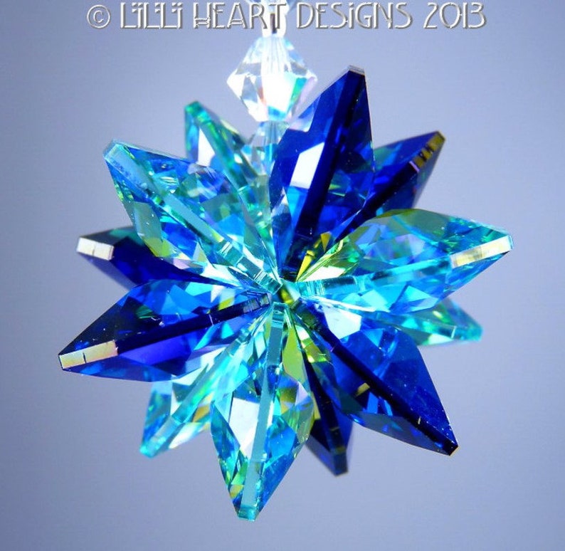 May include: A multi-faceted, star-shaped ornament with a clear, faceted crystal at the top. The ornament is primarily blue and turquoise, with a clear crystal at the top. The text "&copy; LILLI HEART DESIGNS 2013" is visible at the top.