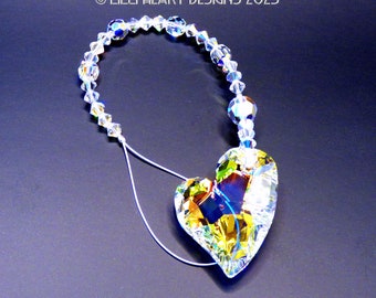 Puede incluir: Un atrapasol en forma de corazón de cristal con un acabado arcoíris iridiscente cuelga de una hebra de cuentas de cristal transparentes. El corazón está suspendido de una cuerda blanca.