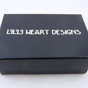 May include: A black box with the text "Lilli Heart Designs" printed in white on the top.