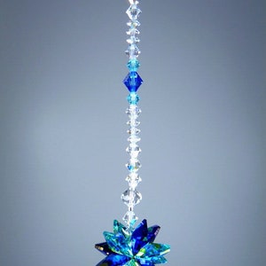 May include: A hanging crystal ornament with a starburst design. The ornament features a string of clear and blue crystals leading to a multi-faceted starburst in shades of blue and green. The text "&copy; Lilli Heart Designs 2013" is visible.