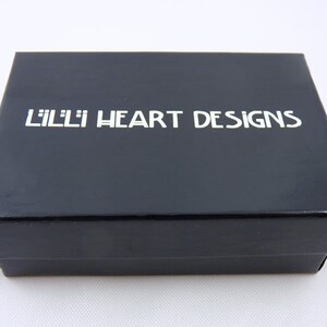 May include: A black box with the text "Lilli Heart Designs" printed in white on the top.