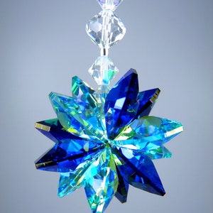 May include: A hanging crystal ornament with a starburst design. The ornament features faceted blue and green crystals arranged in a star shape, with a clear crystal strand above. The text "&copy; LILLI HEART DESIGNS 2013" is at the top.