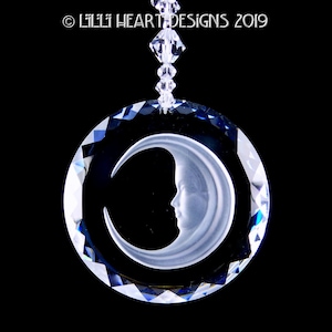 May include: A crystal suncatcher with a crescent moon design. The moon is etched into the crystal and has a white, frosted appearance. The crystal is clear and has a blue iridescent sheen.