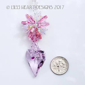 May include: A pink and clear crystal suncatcher with a heart-shaped crystal pendant. The suncatcher is hanging from a silver chain. The image includes the text "Lilli Heart Designs 2017".