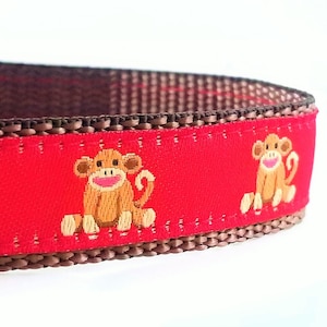 May include: Red dog collar with brown trim and a repeating pattern of brown monkeys with smiling faces.