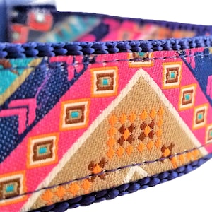 May include: A close-up of a blue, pink, orange, and brown patterned dog collar. The collar is made of a woven fabric with a geometric design.