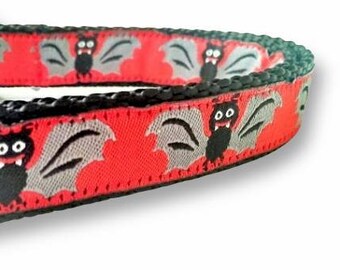 May include: Red and black pet collar with a repeating pattern of cartoon bats with gray wings. The collar has a black border and a green attachment loop.