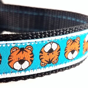 May include: A blue and white dog collar with a repeating pattern of orange tiger faces. The collar is made of black nylon webbing.