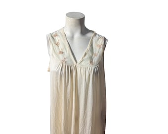 May include: Cream-colored sleeveless nightgown with a V-neckline. The bodice features delicate floral embroidery in a light brown hue. The fabric drapes softly, creating a flowing silhouette. A vintage-inspired sleepwear item.