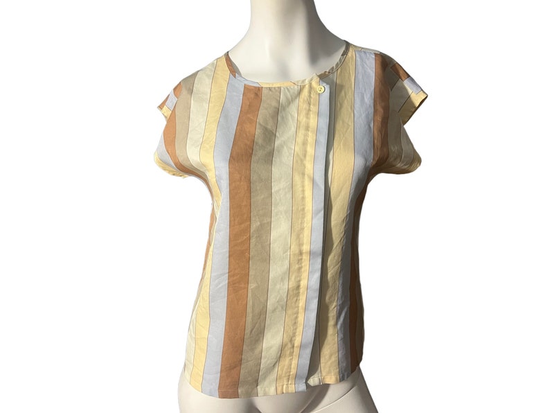 May include: A striped short-sleeved blouse with a button closure at the neck. The blouse is made of a light-weight fabric and has a relaxed fit. The colors are a mix of light blue, beige, and brown.