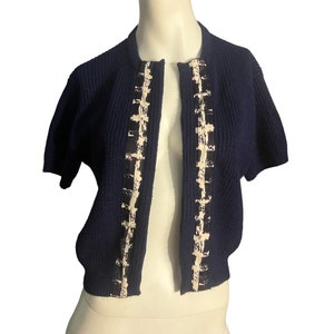 Pode incluir: Um cardigan azul marinho de manga curta com uma guarnição branca e preta na frente.
