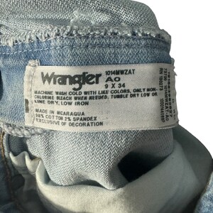 May include: A close-up of a blue denim Wrangler jeans label with the text "1014MWZAT Ao 9 X 34" and care instructions. The label also states "Made in Nicaragua 98% Cotton 2% Spandex Exclusive of Decoration."