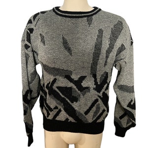 Puede incluir: Un suéter con estampado gris y negro. El suéter tiene cuello redondo y mangas largas con puños negros. El diseño incluye formas geométricas en negro sobre un fondo gris. El dobladillo y el cuello son negros.
