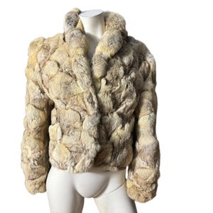May include: A cropped fur jacket with a collar. The jacket is made of a light brown fur with a patchwork design.
