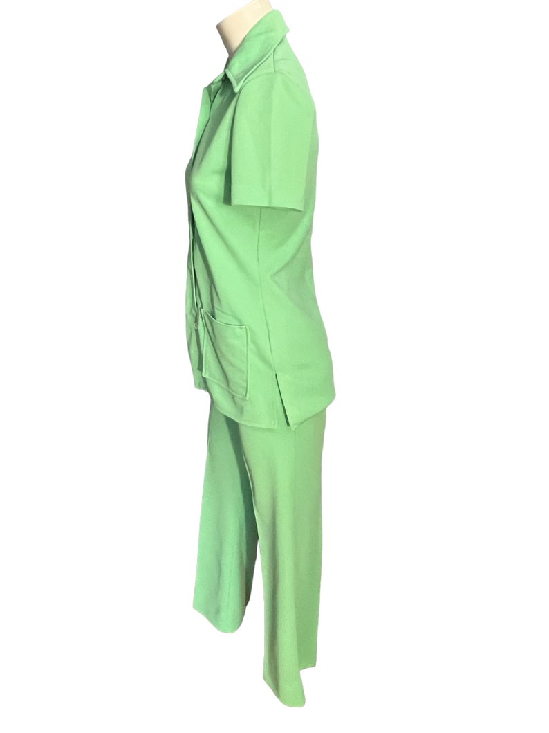 May include: A light green two-piece suit. The short-sleeved collared shirt has two front pockets and buttons down the front. The matching pants are wide-legged. The suit is displayed on a mannequin.